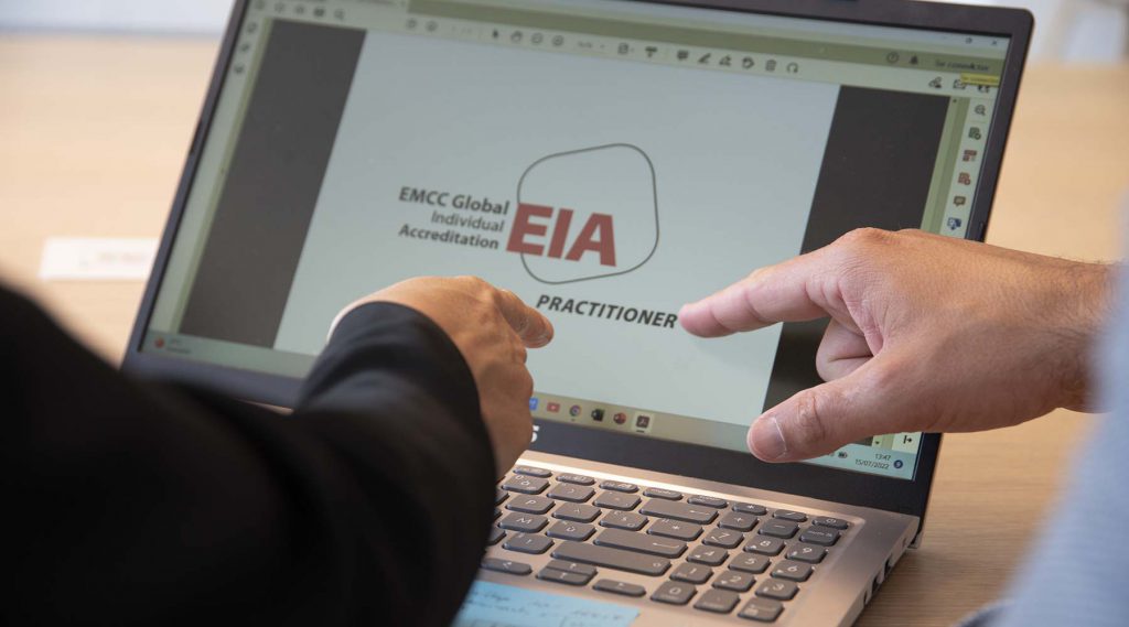 Gros plan sur des mains montrant le logo de la certification EMCC sur un écran d'ordinateur.